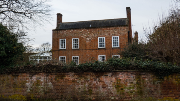 Front of red brick house with major repair visible to the front behind a red brick wall