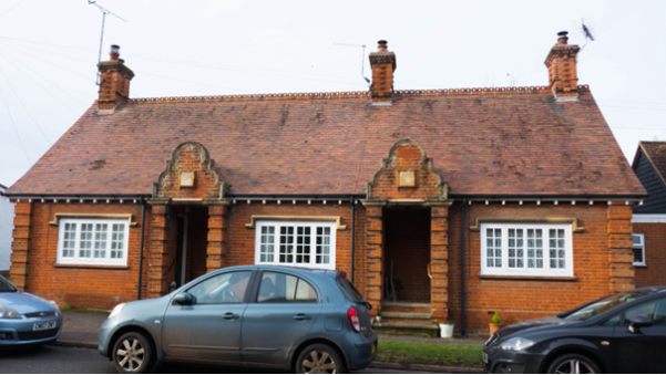 Pretty single storey red brick almshouses with attractive gables over the two front doors and decorative ridge tiles