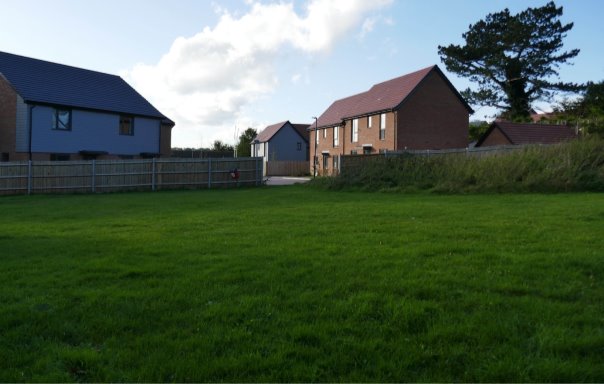 Informal grass space with fence around and houses behind