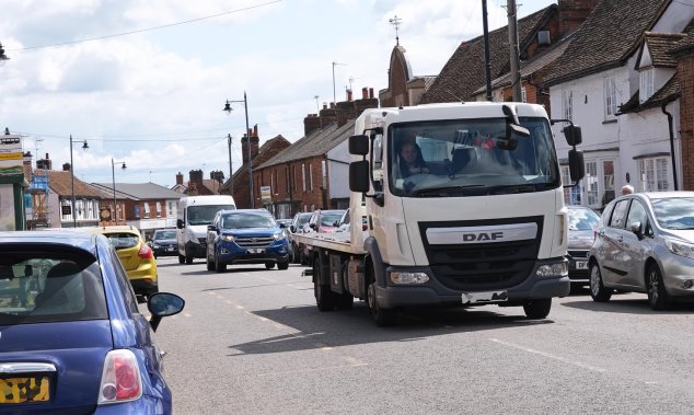 A busy High Street with cars parked on both sides and only room for cars to travel in one direction