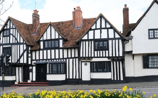 Old timber frames and white plastered 4 bay building with daffodils in foreground