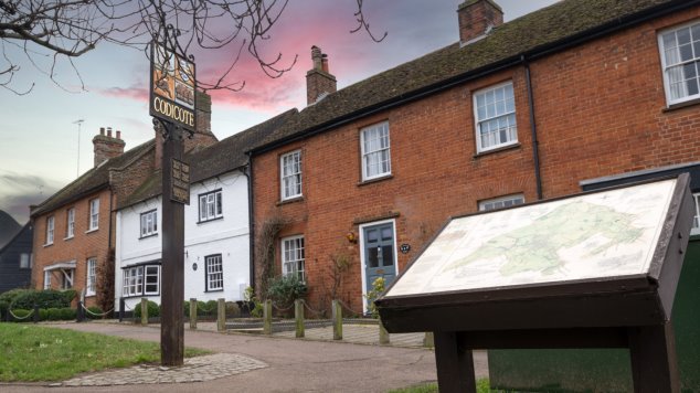 Codicote village sign on the village green with historic housing behind and information road about the village in the foreground