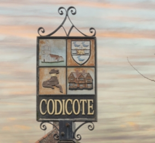 Close-up of the village sign which is divided into four images with Codicote beneath and decorative ironwork 